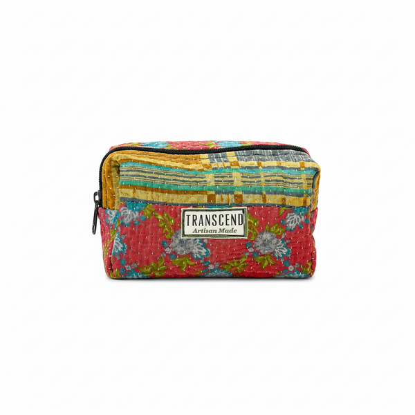 A rectangular zippered pouch with a colorful patchwork quilted fabric design, featuring a red floral pattern on the bottom, yellow and blue striped patterns on the top, and a central white brand label that reads 'TRANSCENO Artisan Made'.