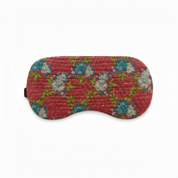 A quilted fabric sleep mask with a red background and a floral pattern in blue, white, and green, shown on a plain white background.