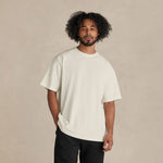 Man wearing a white t-shirt and black pants standing against a beige background 13