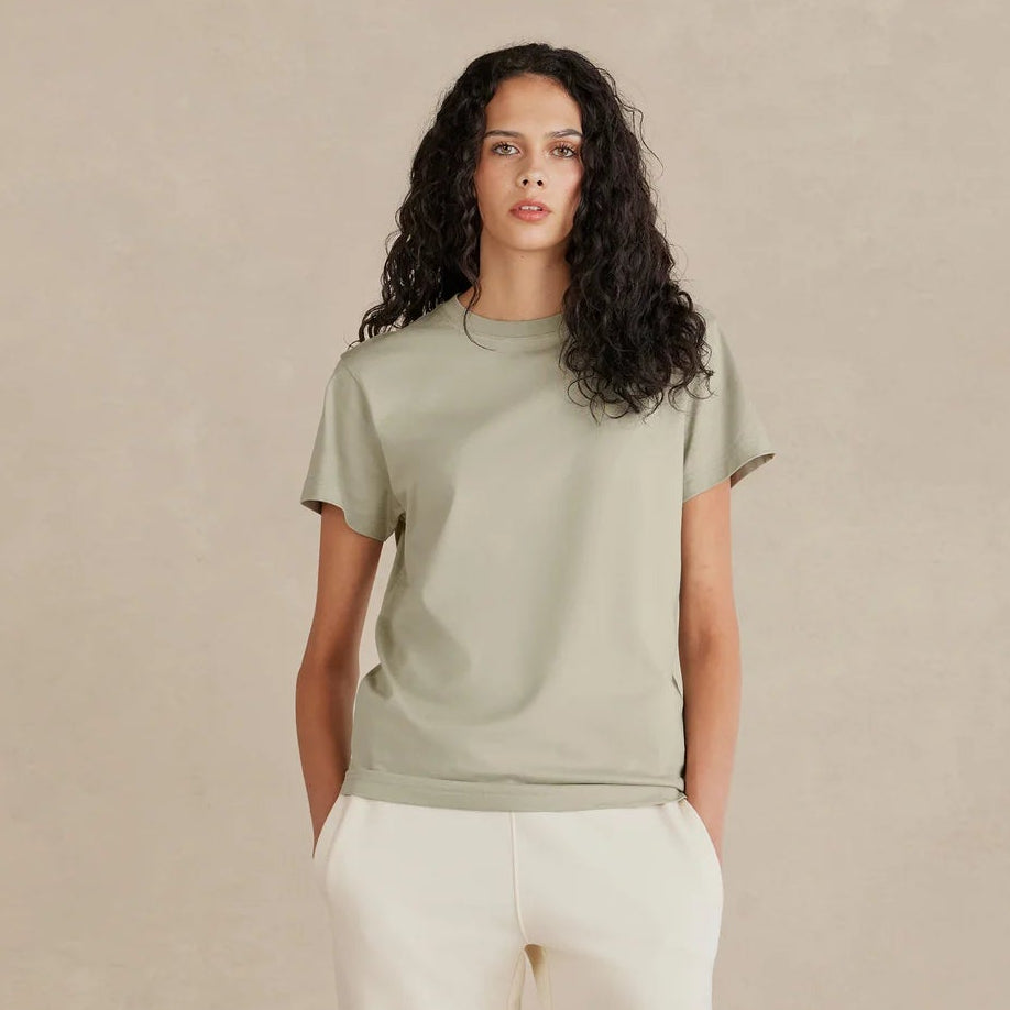 Woman wearing a green t-shirt and white pants against a beige background