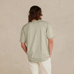 Person wearing a light green t-shirt and white pants standing against a beige background 9