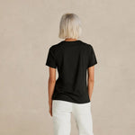 Person wearing a black t-shirt and white pants on a beige background 2