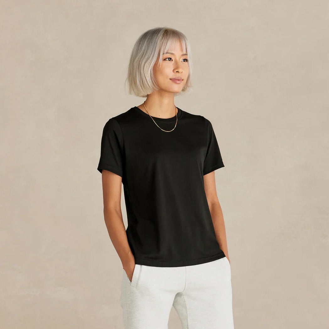 Person wearing a black t-shirt and white pants on a beige background