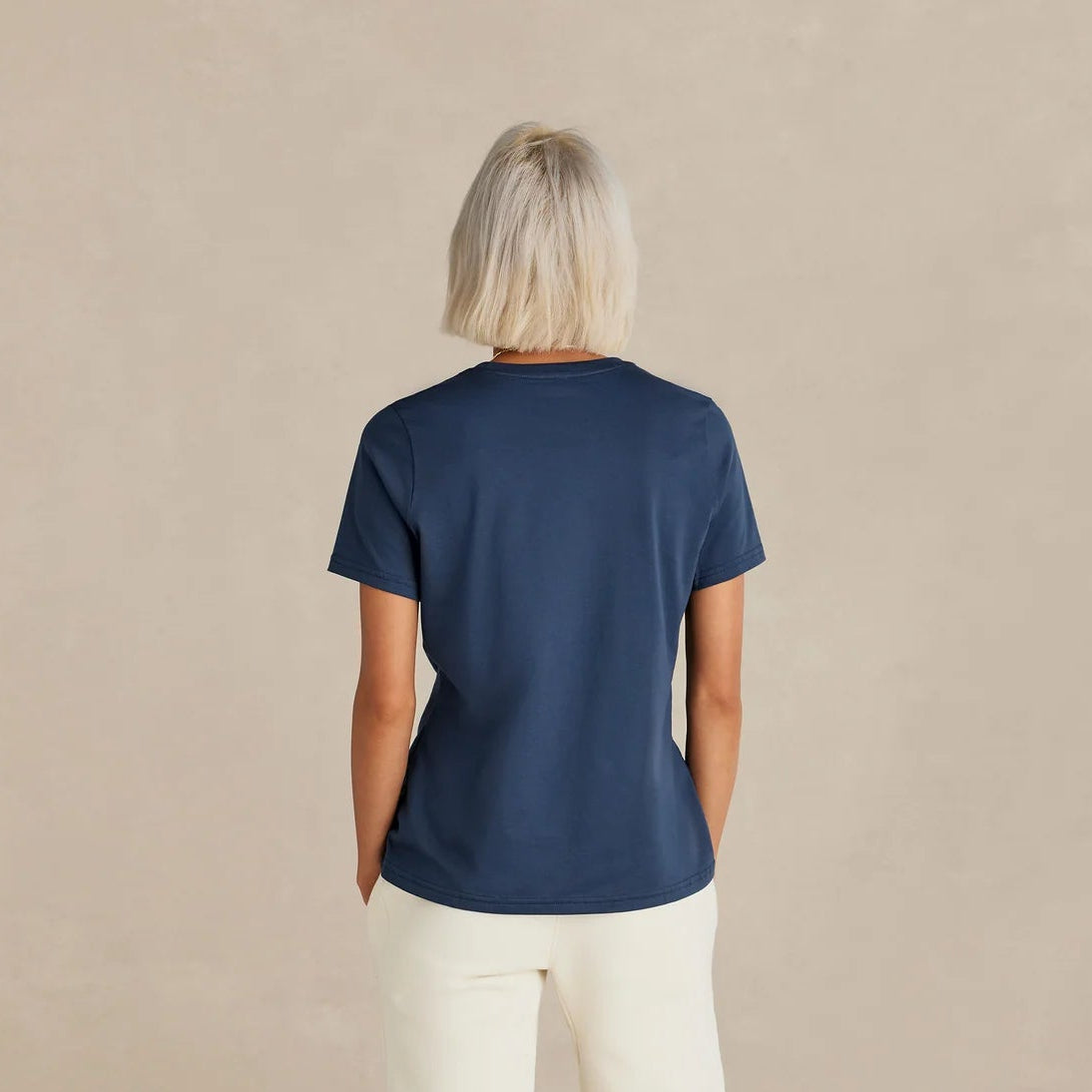 Person wearing a navy blue t-shirt and white pants standing against a beige background