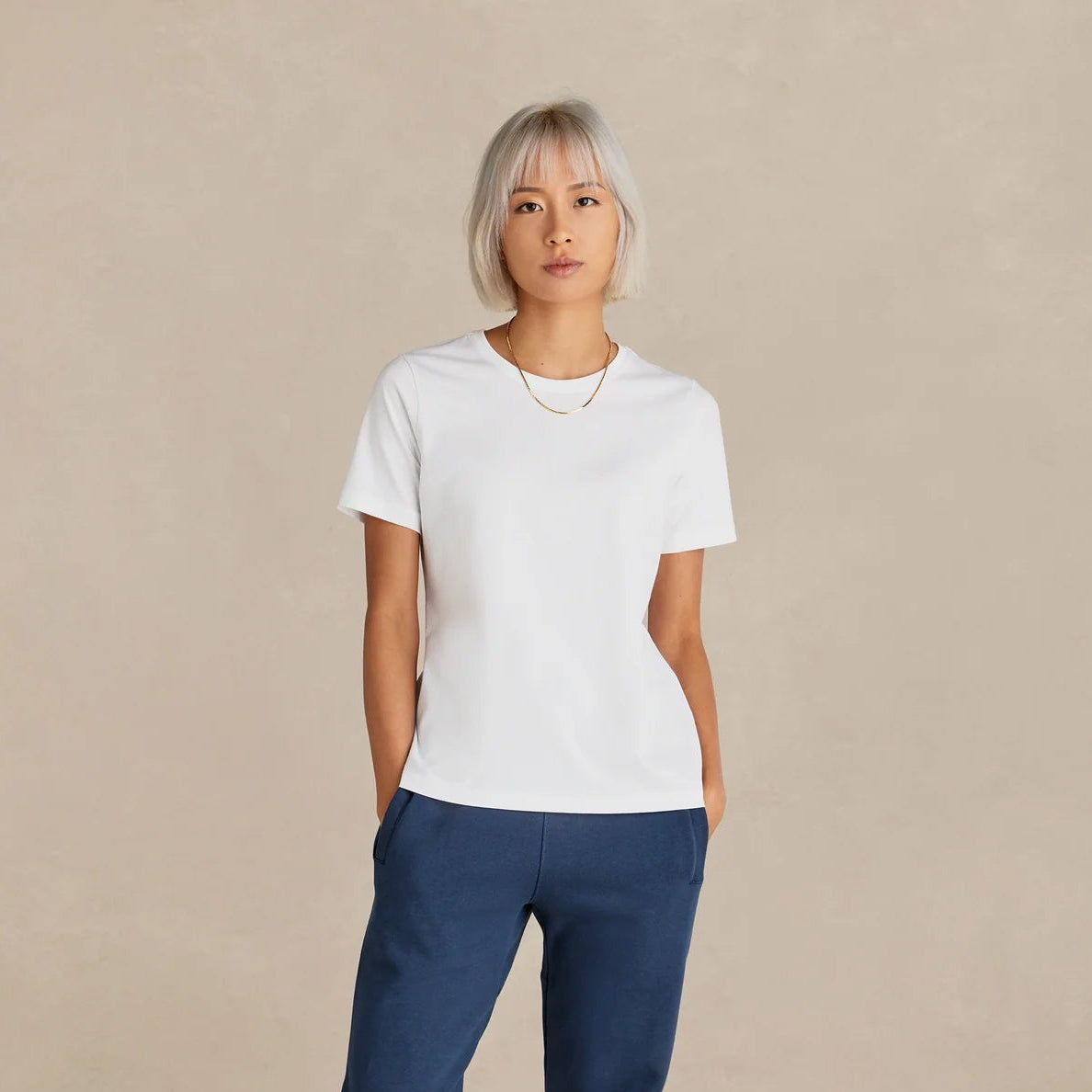 Person wearing a white t-shirt and blue pants on a beige background