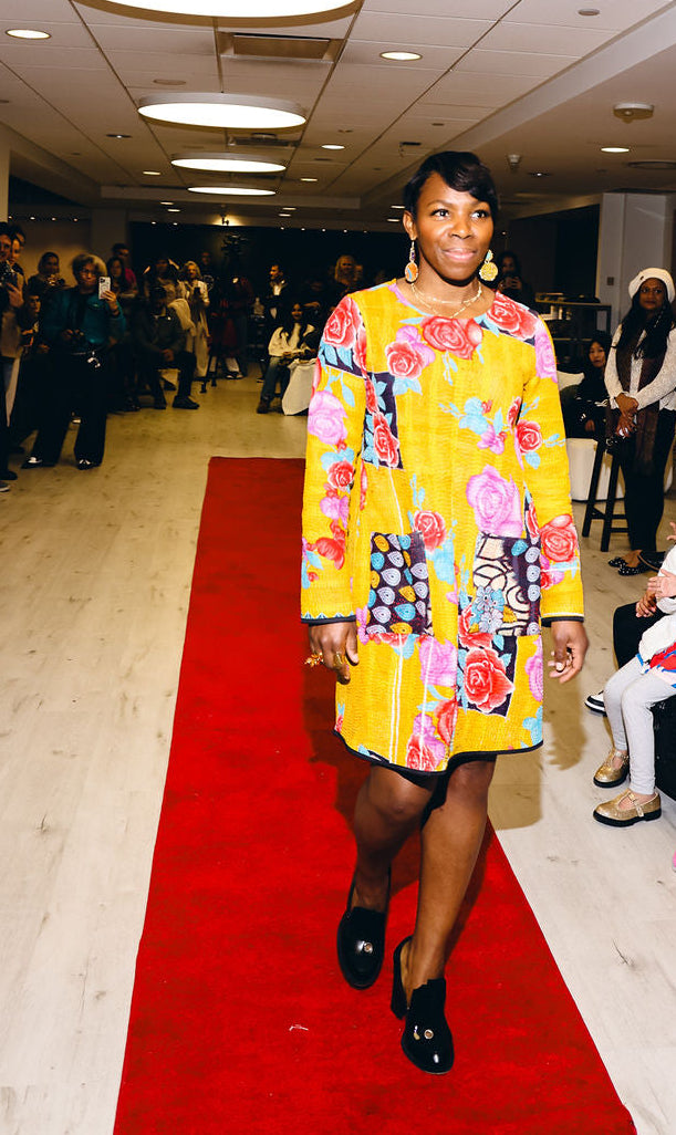 Woman in a colorful dress walking on a red carpet at an event.